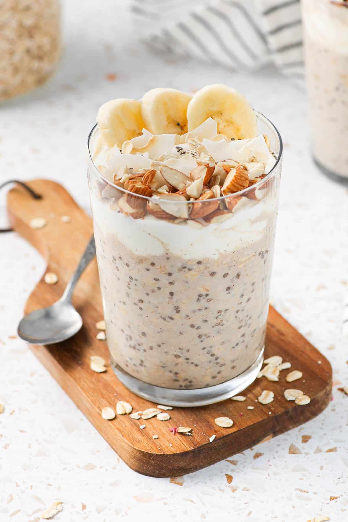 a glass of overnight oats with banana, almonds, and coconut.