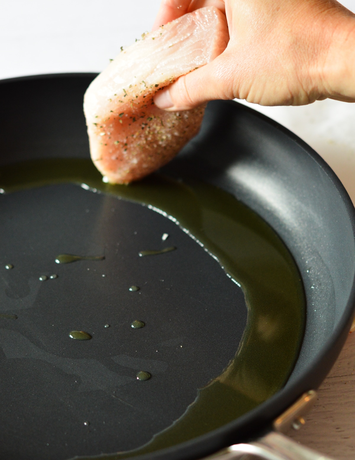 hand putting swordfish into a skillet with oil.