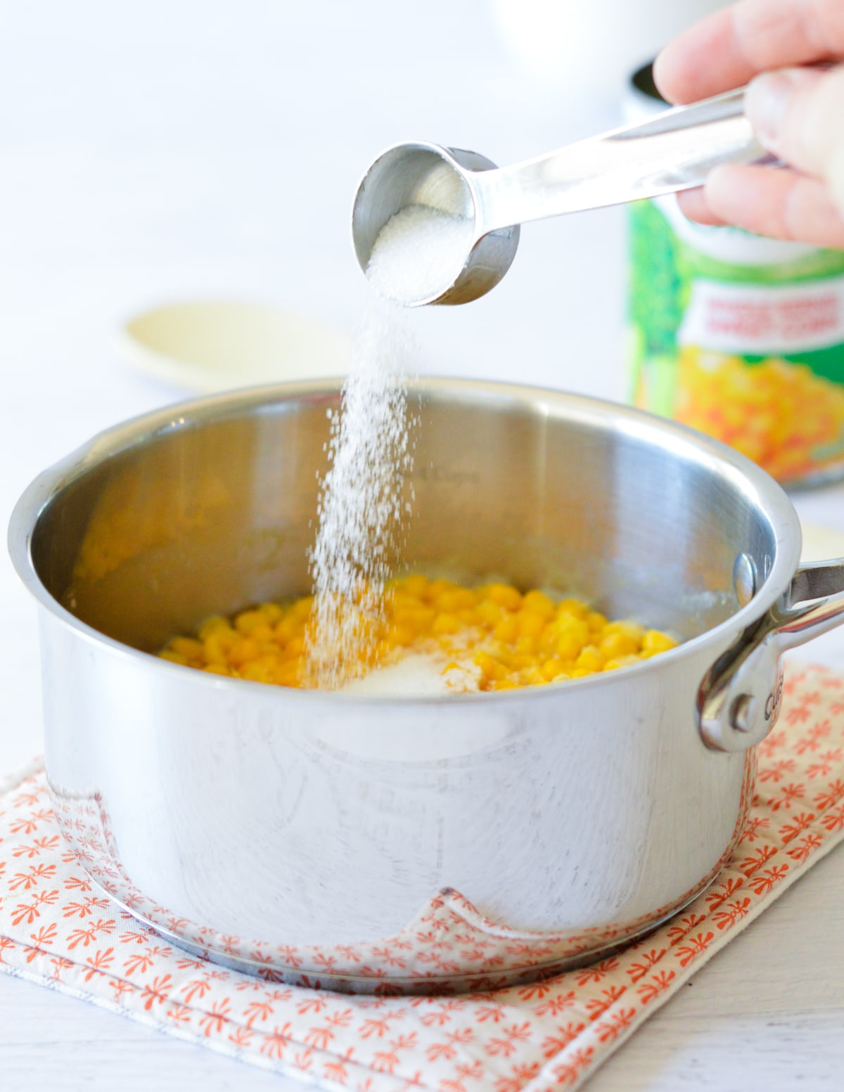pouring sugar into a saucepan with corn.
