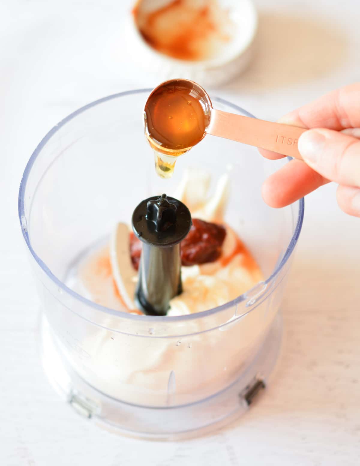 pouring honey into a food processor with mayo and chipotles. 