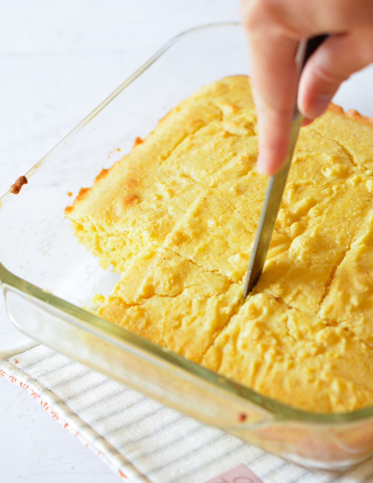 hand cutting cornbread into slices with a knife.