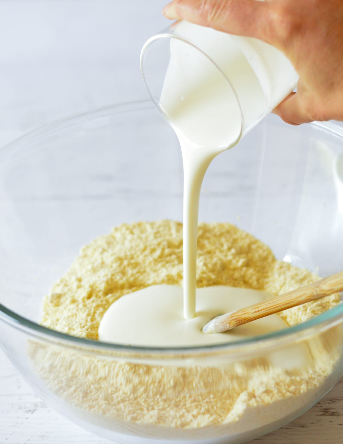 hand pouring buttermilk into a bowl with cornmeal
