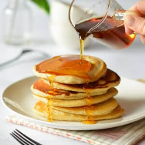 pouring maple syrup onto pancakes.