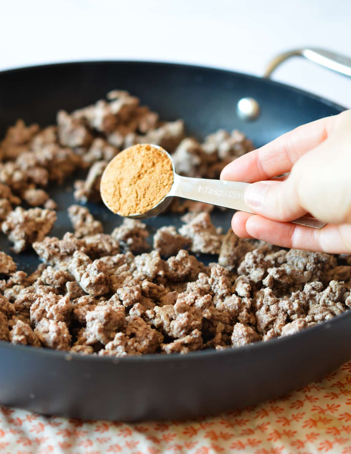 hand adding taco seasoning to meat. 