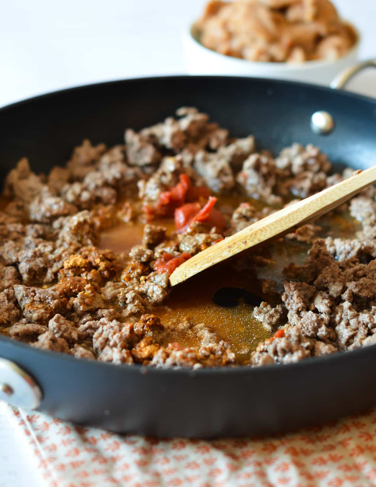 ground beef, seasoning, tomato paste, and water in a skillet with a spatula.