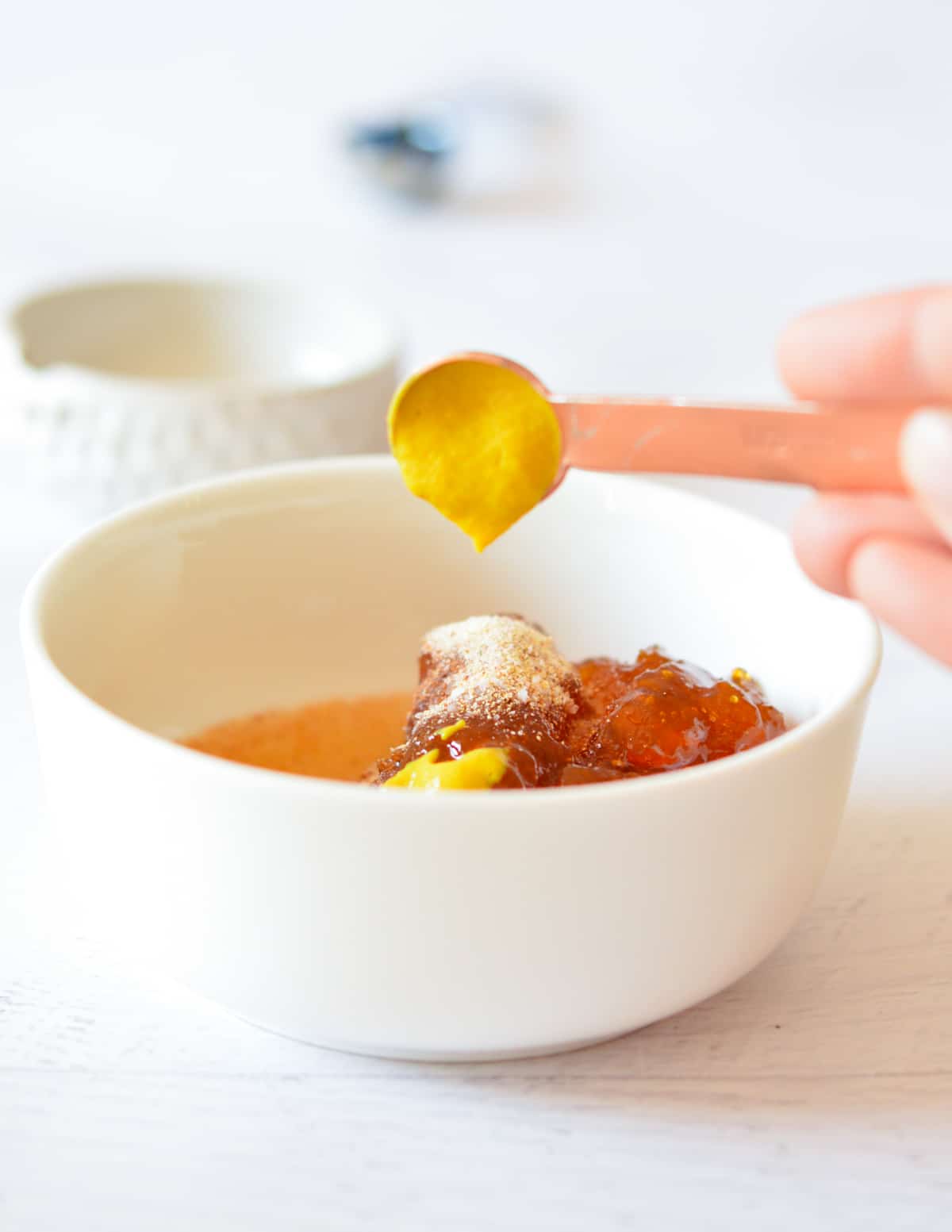 hand pouring mustard into a bowl with apricot jam, spices, and pineapple juice.