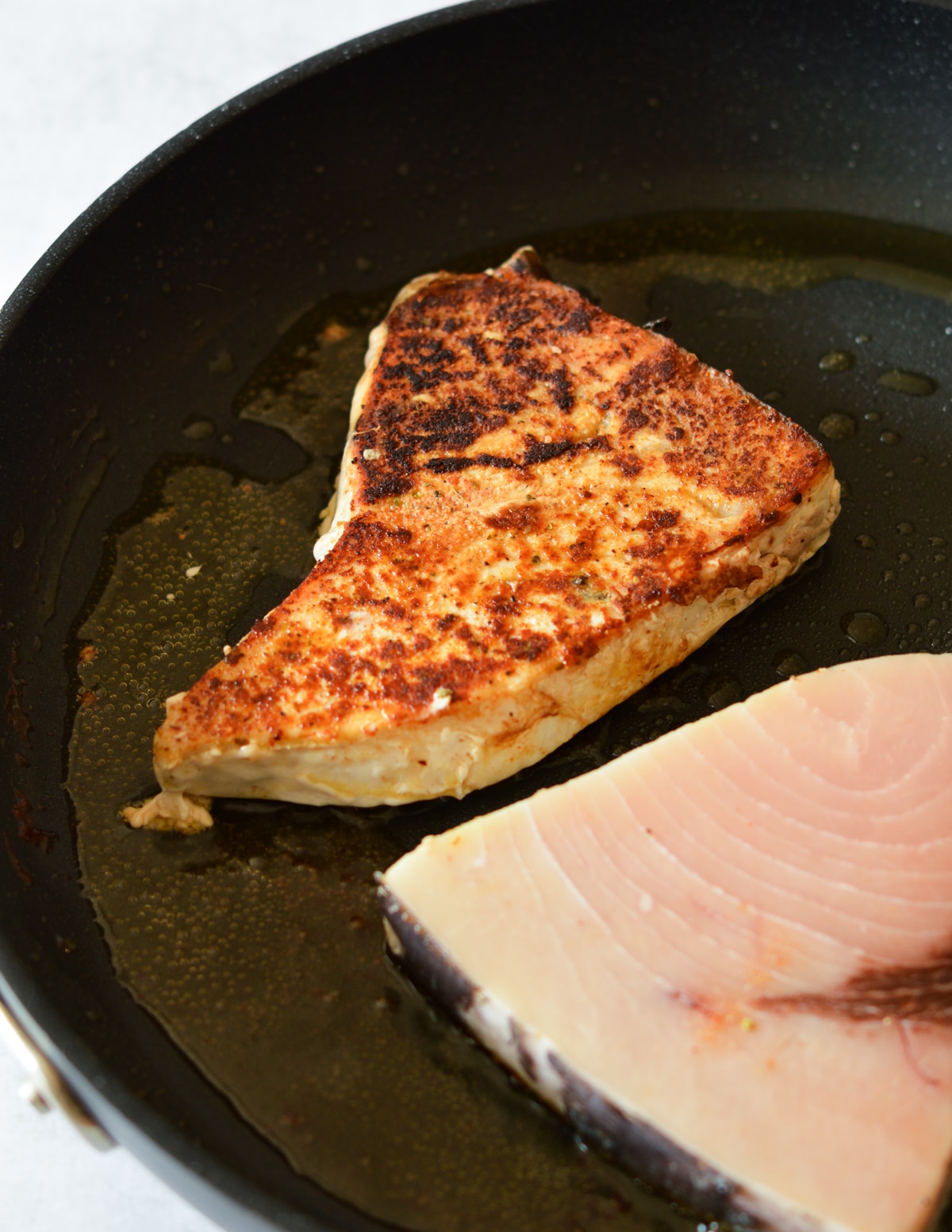 caramelized swordfish in a skillet with olive oil.