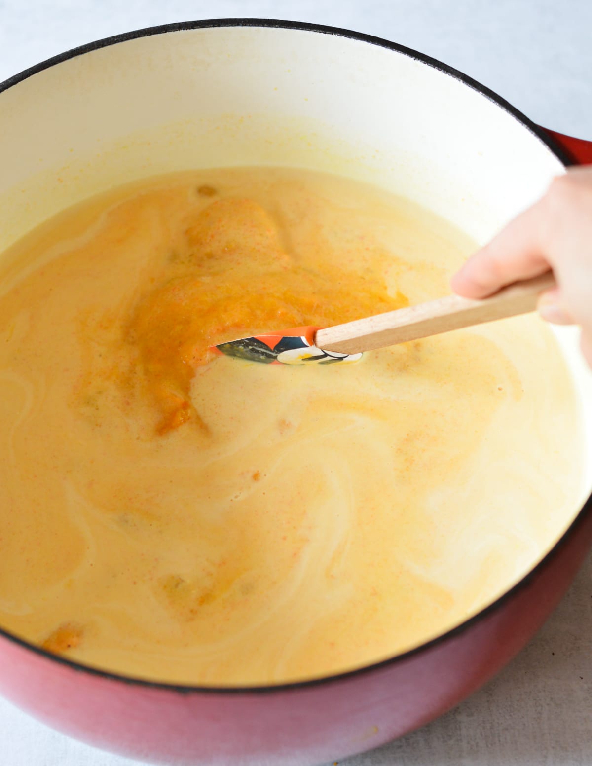 stirring cream into butternut squash soup with a spatula.