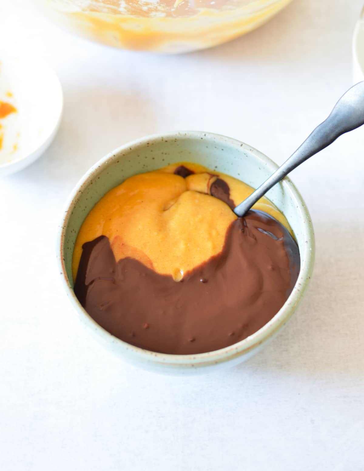 a bowl of pumpkin batter and melted chocolate with a spoon in it.