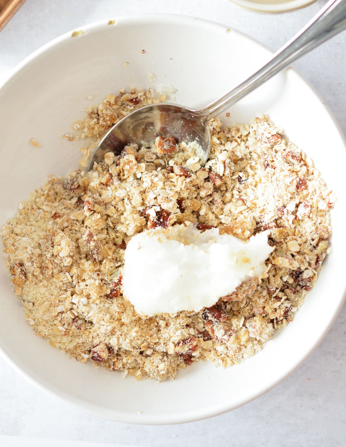 a bowl of oats, sugar, and pecans, with coconut oil on top.