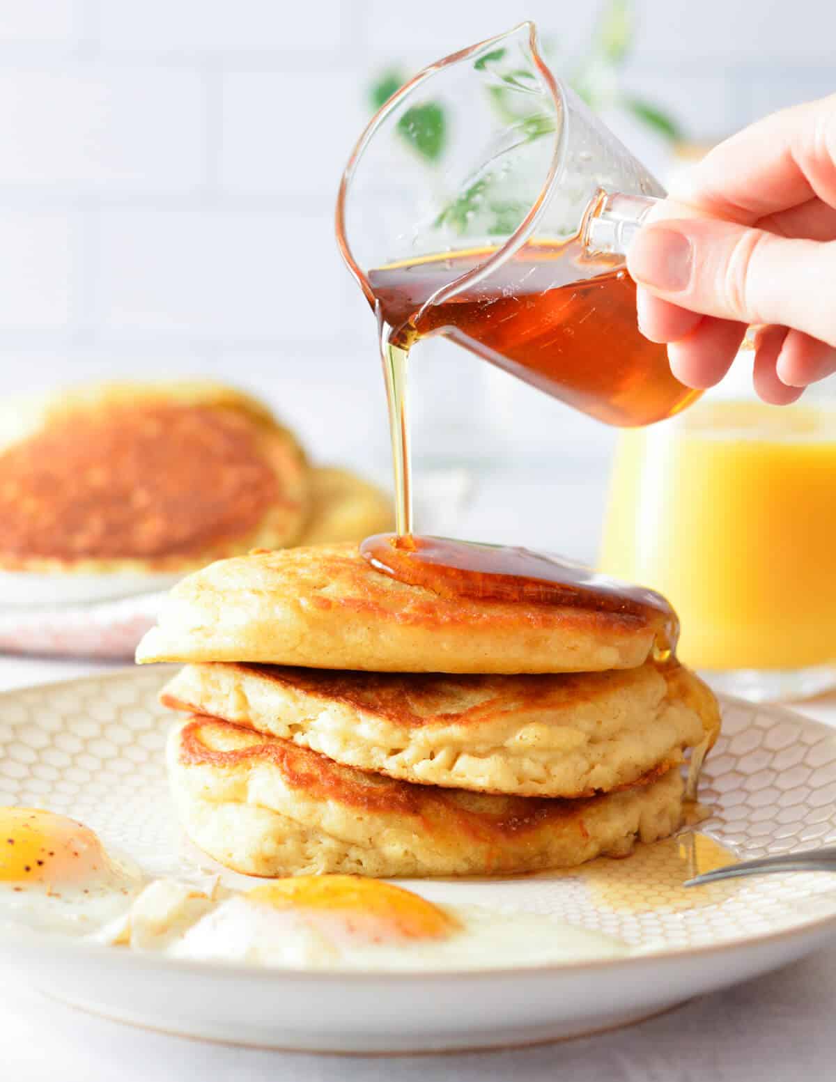 pouring maple syrup onto a stack of pancakes.