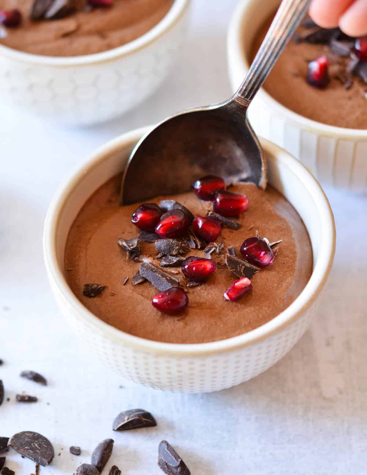 spoon in a cup of chocolate mousse with pomegranate seeds on top.