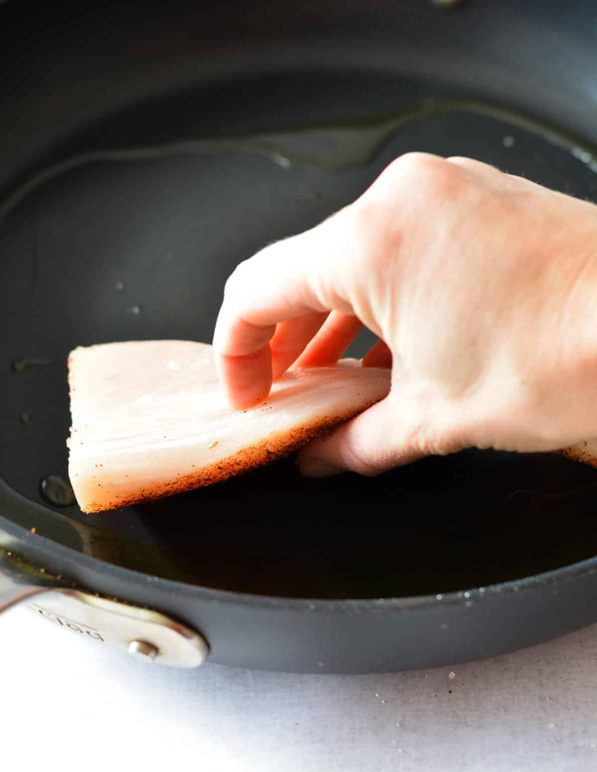 hand placing a mahi fillet into a hot skillet.