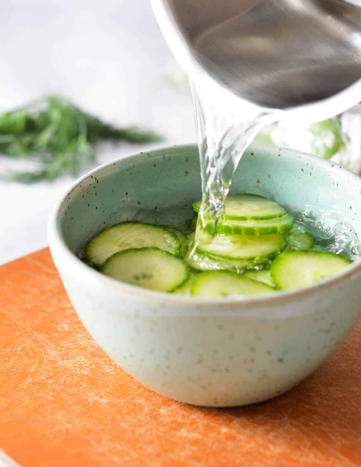 pouring hot vinegar over cucumber slices.