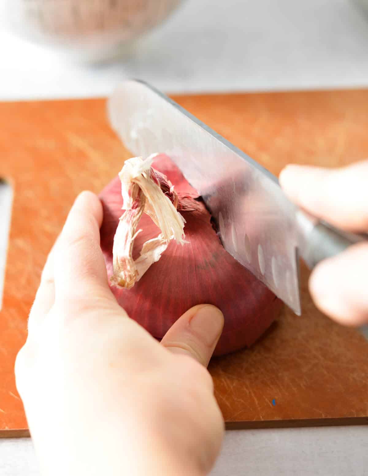 someone cutting a red onion in half.