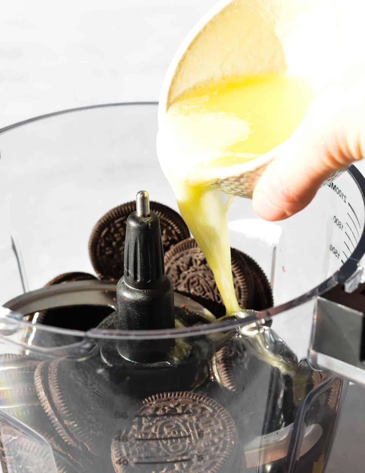 pouring butter into a food processor with Oreos. 