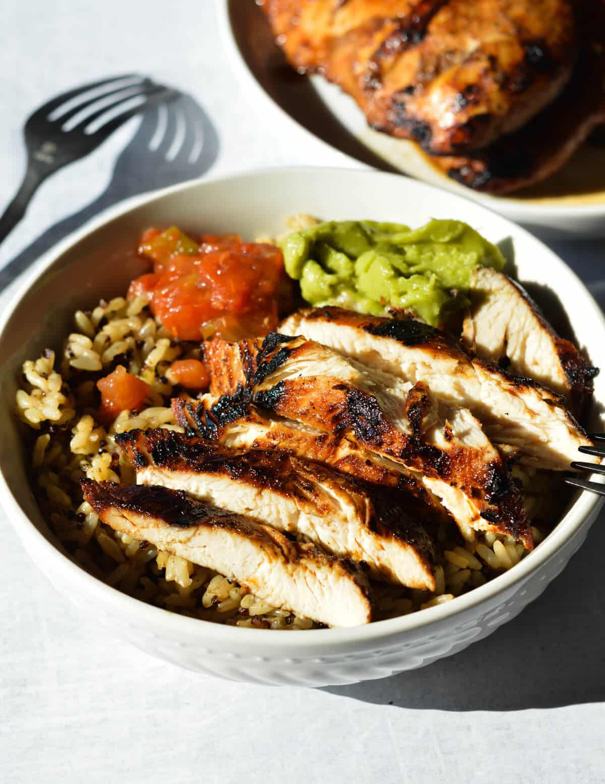 a bowl of sliced grilled chicken with rice, guacamole, and salsa. 