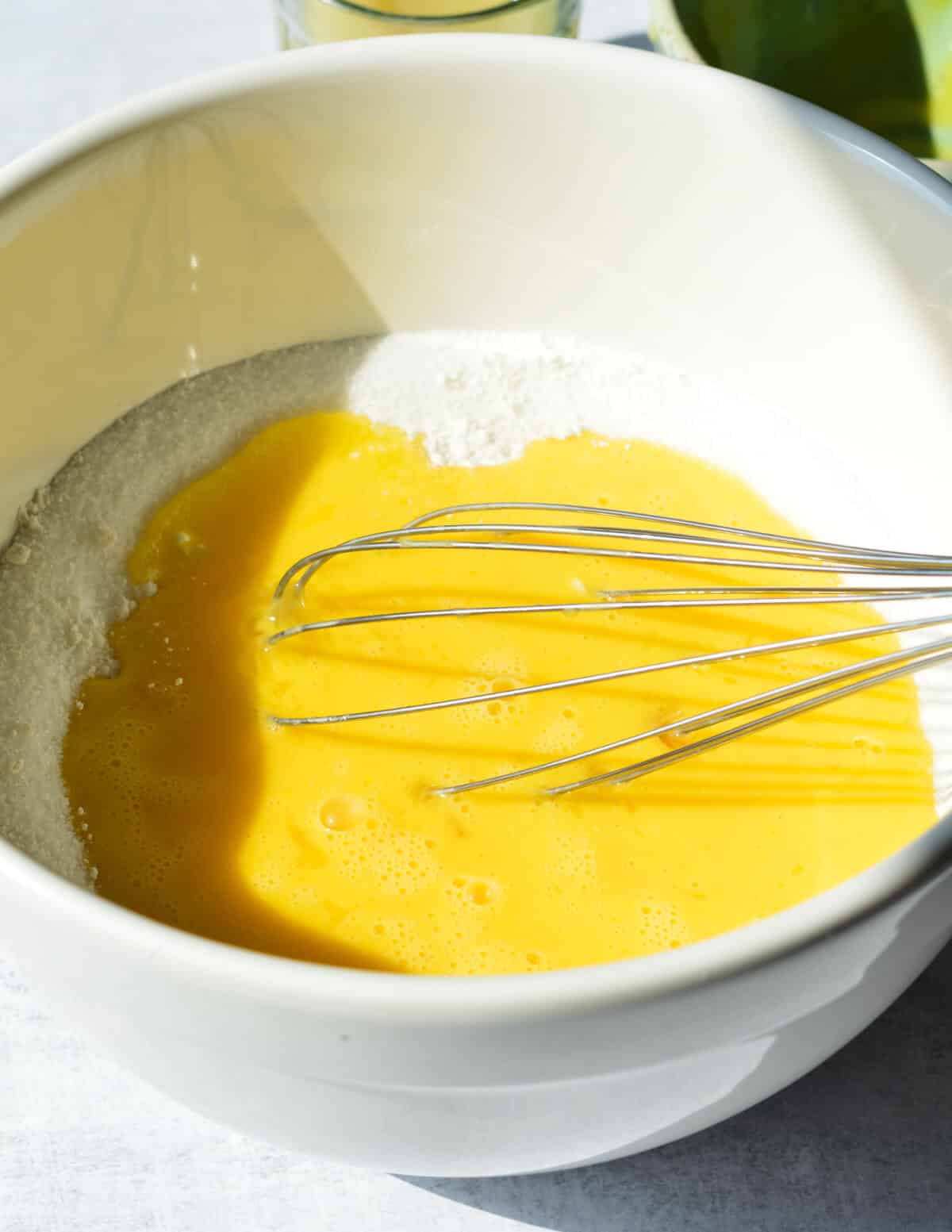 a bowl of sugar with eggs and a whisk.