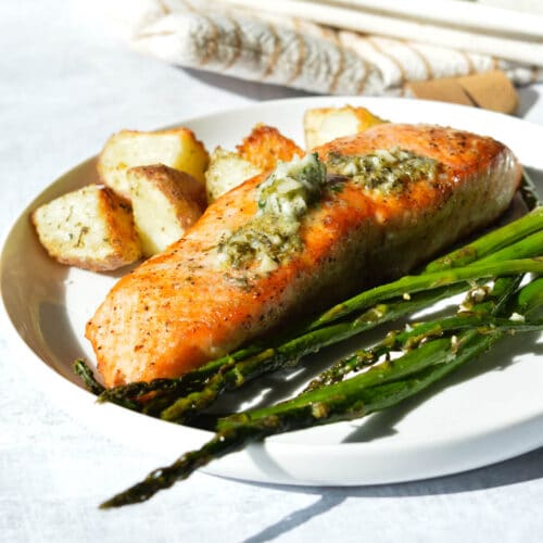 salmon with herb butter, asparagus, and potatoes on a plate.