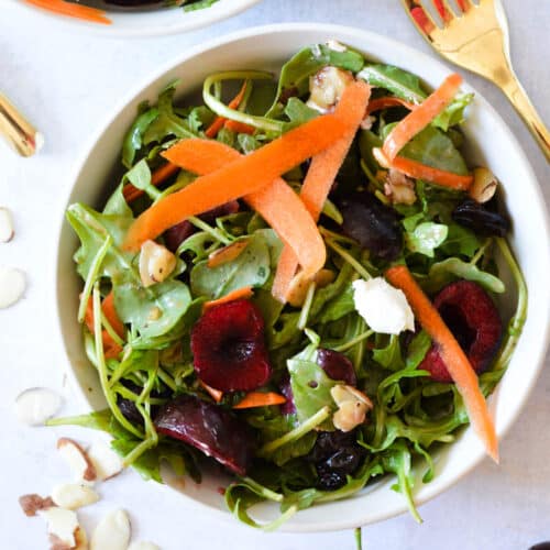 a bowl of arugula salad with cherries, shaved carrots, feta, and balsamic.