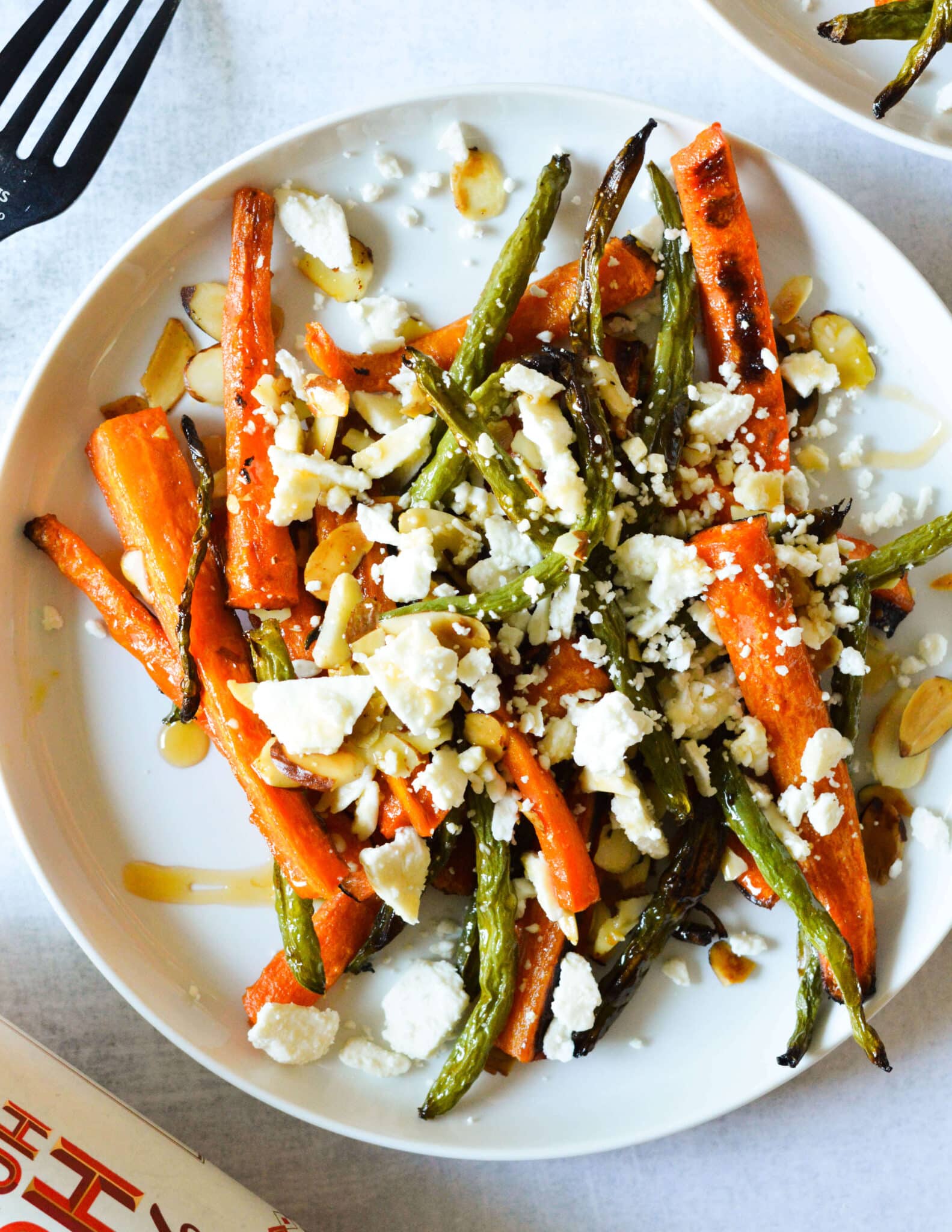 a plate with roasted carrots and green beans, feta, toasted almonds, and hot honey.
