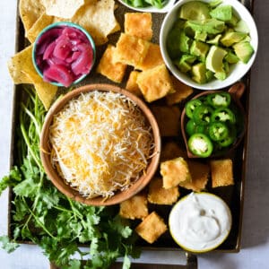 cheese, sour cream, cornbread, avocado, pickled red onions, and tortilla chips on a platter.