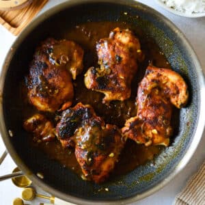blackened chicken thighs in a skillet with mustard sauce.