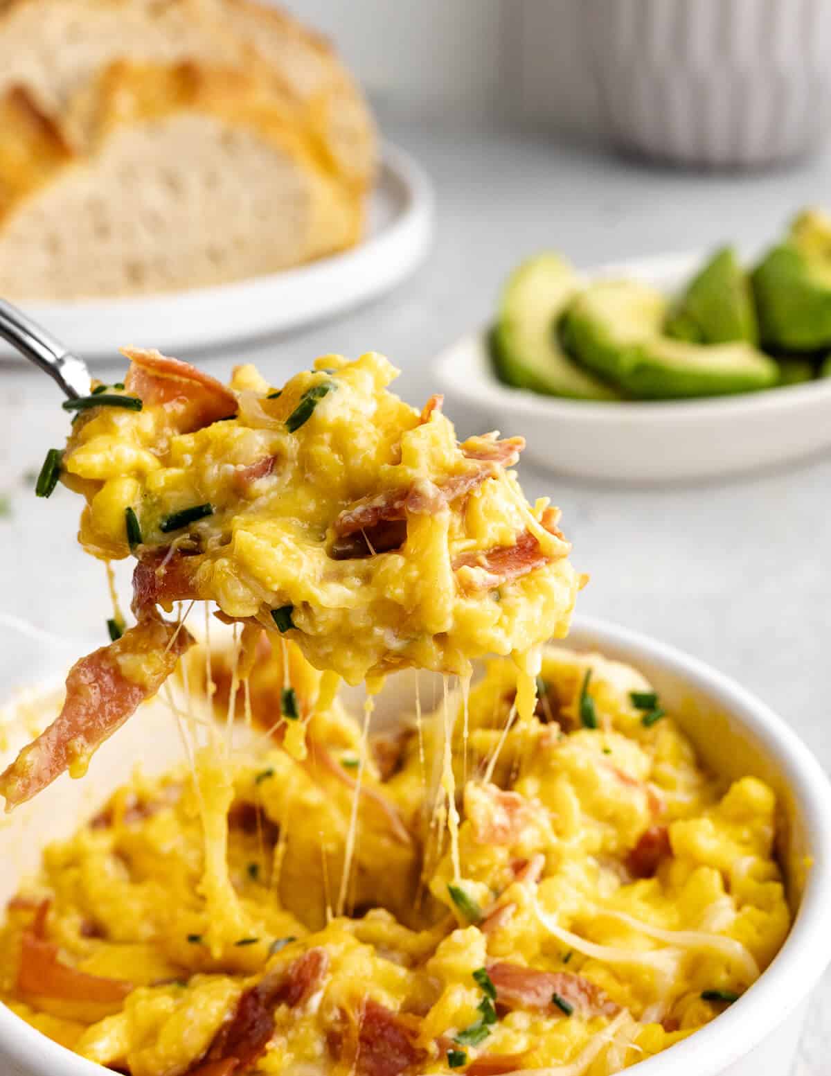 a large bite of cheesy eggs with prosciutto and chives