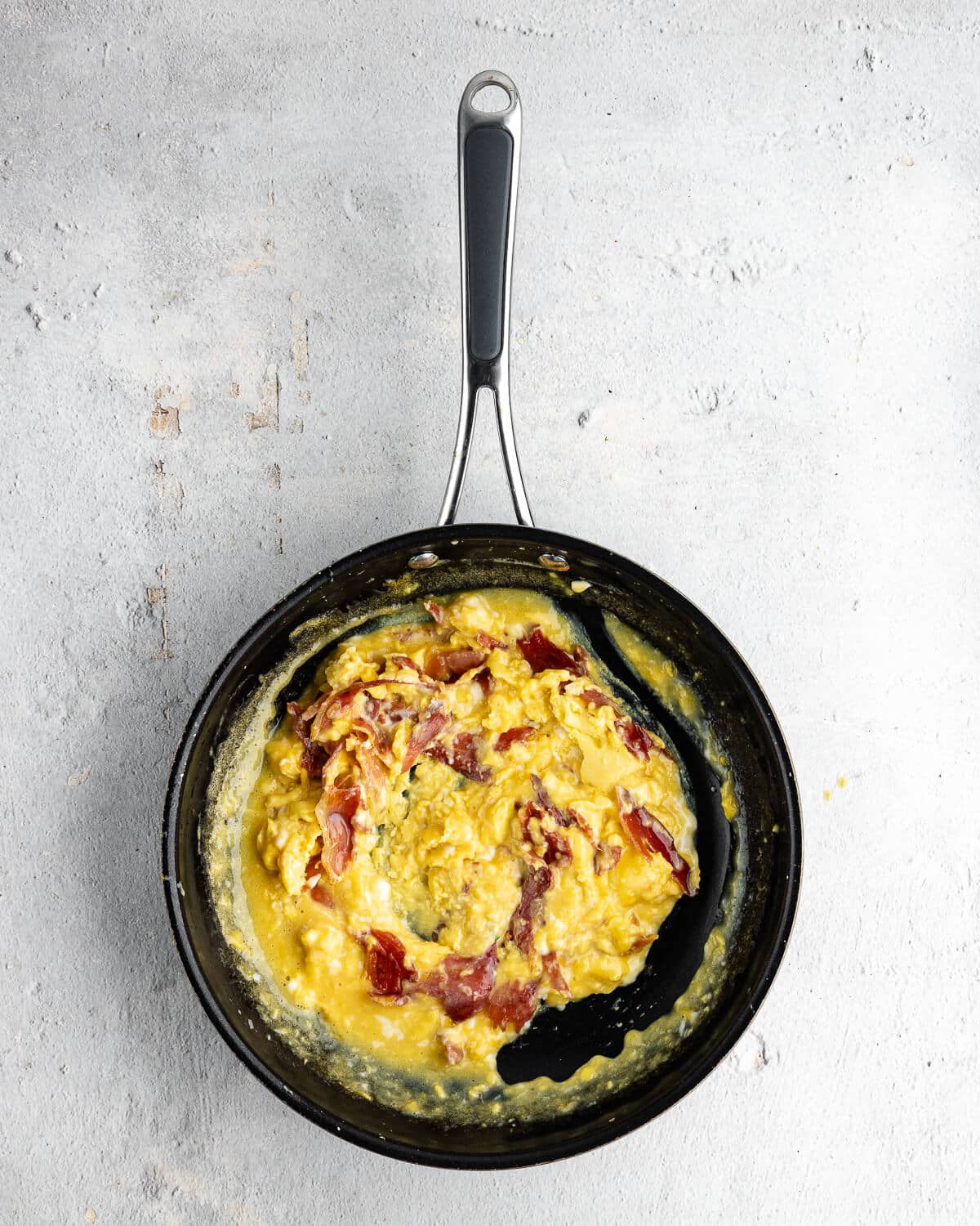 scrambled eggs mixed with crispy prosciutto in a skillet