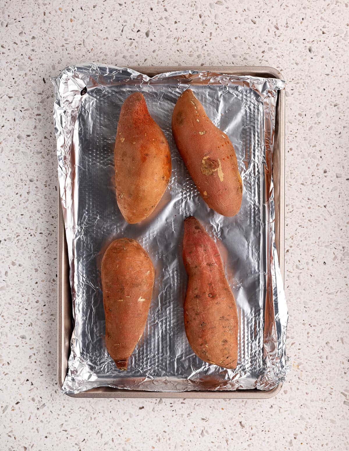 sweet potatoes on an aluminum foil lined sheet pan.