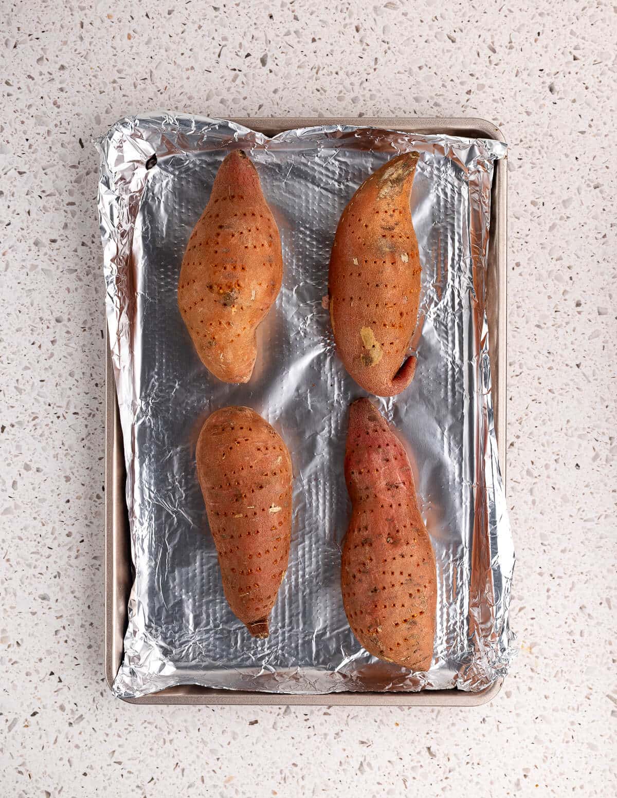 pricked sweet potatoes on an aluminum foil lined sheet pan.