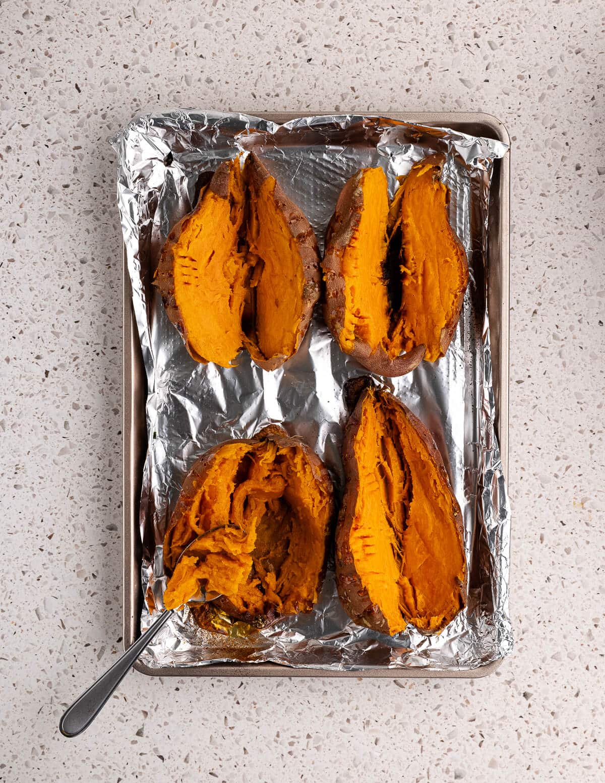baked sweet potatoes cut in half on a sheet pan.