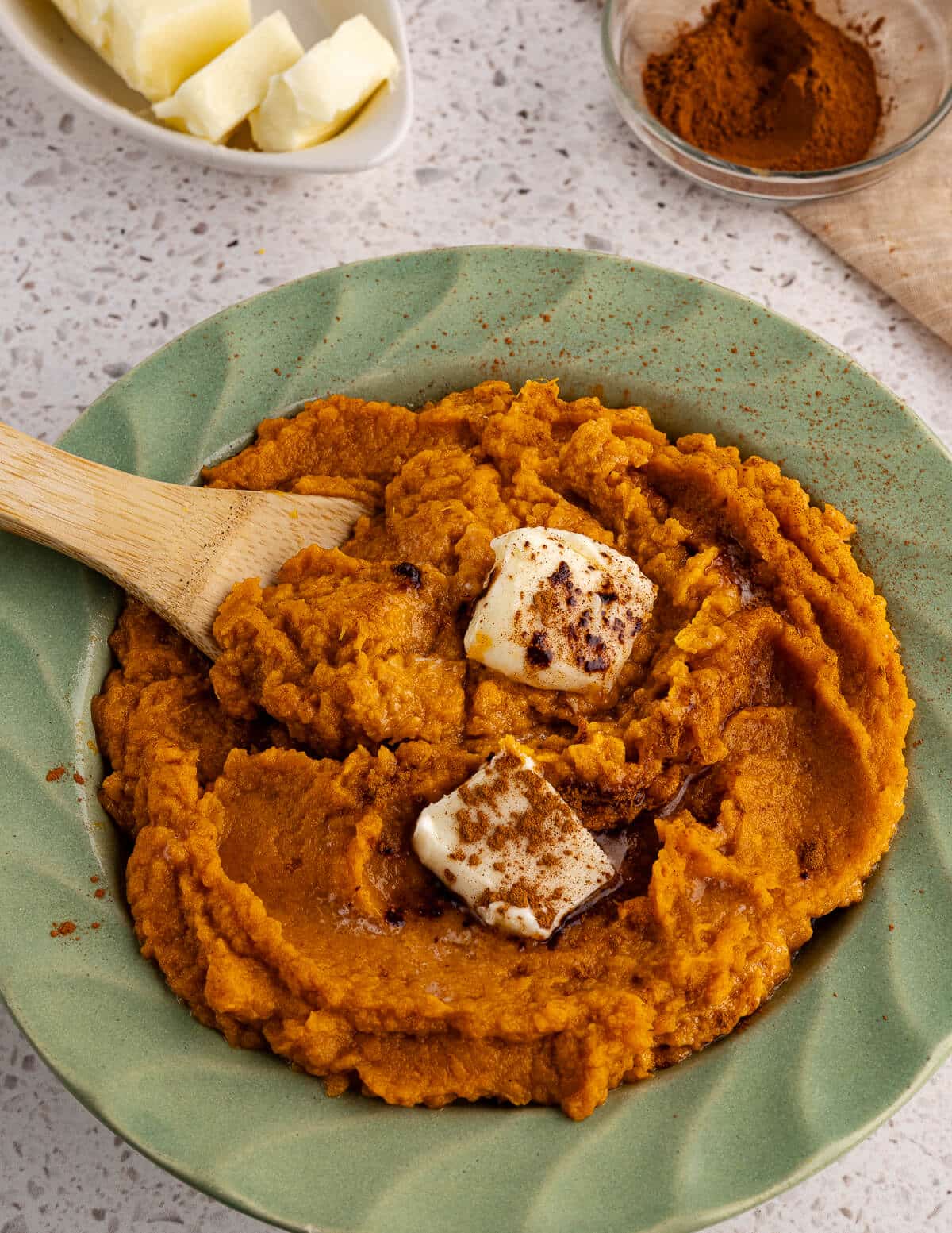a bowl full of mashed sweet potatoes with maple syrup, butter, and cinnamon on top.