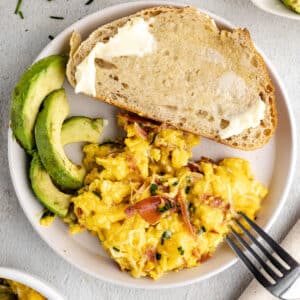 a plate with scrambled eggs, sliced avocado, and buttered toast.