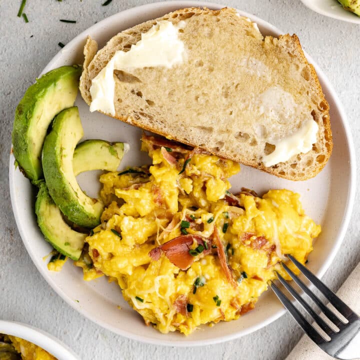 a plate with scrambled eggs, sliced avocado, and buttered toast.