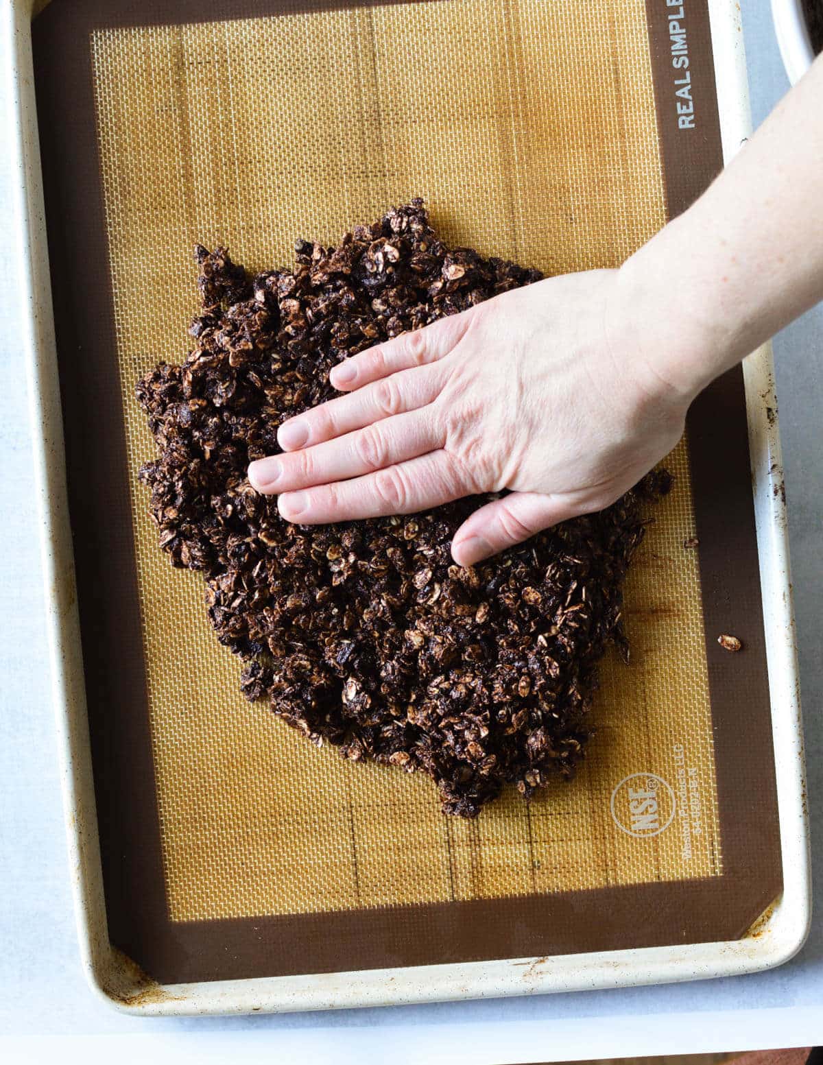 hand pressing chocolate granola mixture down on a pan.