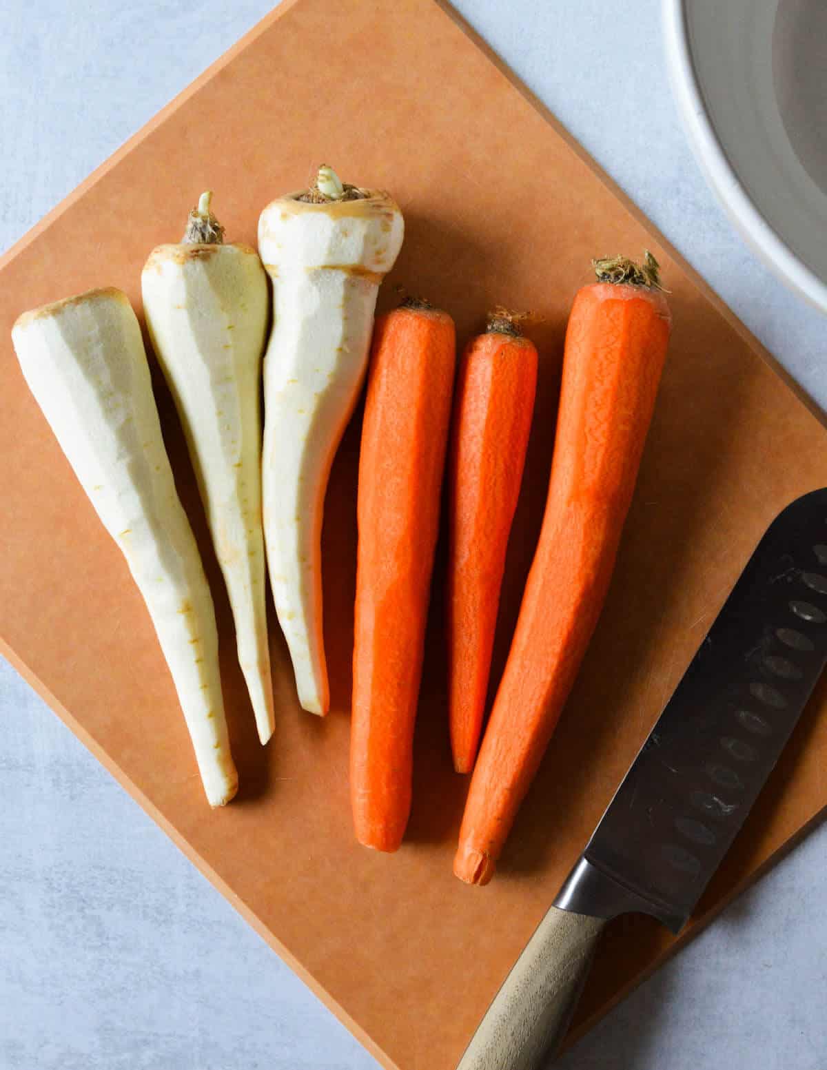 carrots and parsnips on a cutting board with a knife.