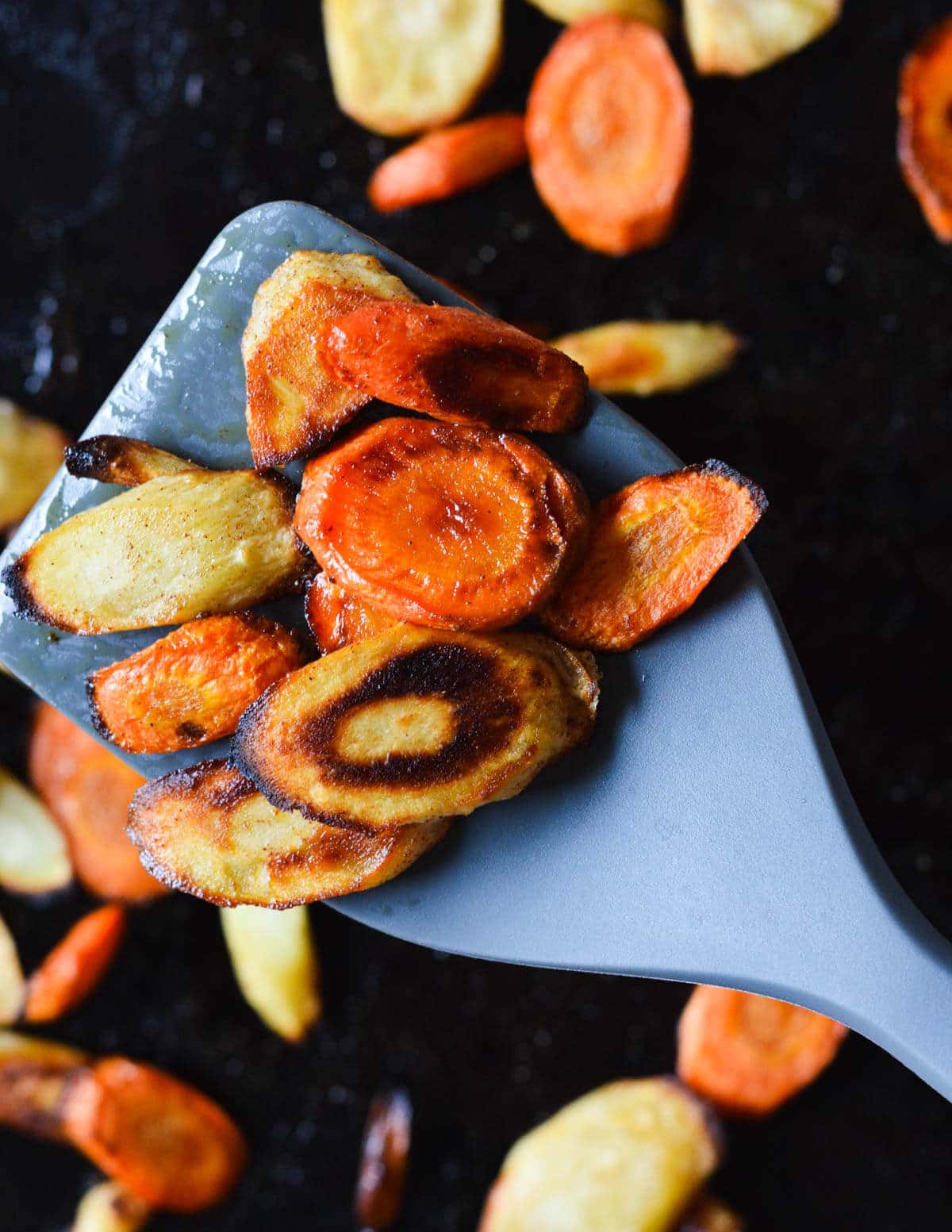 close up of roasted carrots and parsnips on a rubber spatula.
