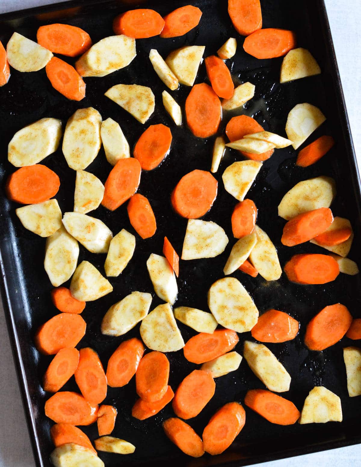 sliced carrots and parsnips coated in a honey olive oil mixture and spread out on a sheet pan.