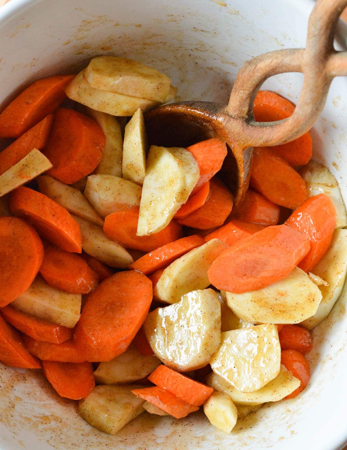 a bowl of sliced carrots and parsnips coated in a cinnamon honey and olive oil mixture.