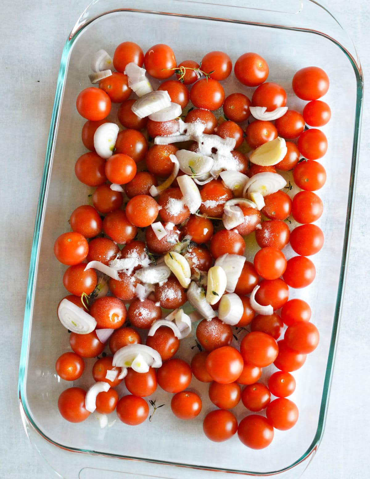 cherry tomatoes, garlic, shallots, olive oil, sugar, and thyme leaves in a glass baking dish.