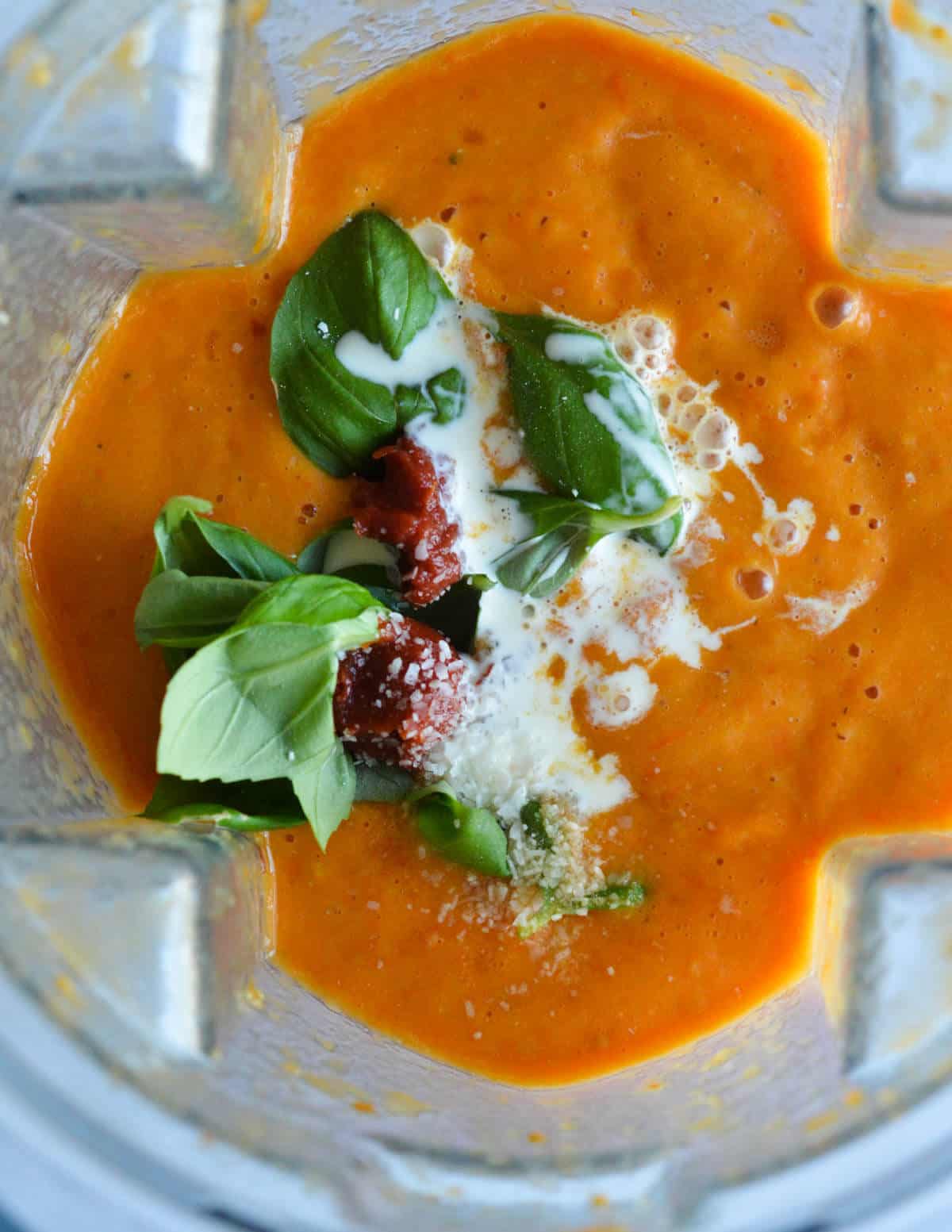 tomato soup in a blender with basil, heavy cream, and tomato paste on top.
