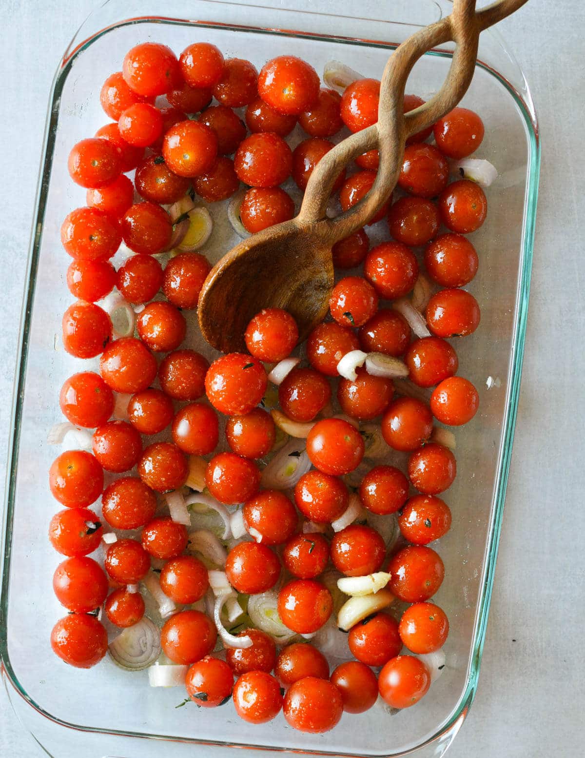 glass baking dish with cherry tomatoes, shallots, and garlic coated in olive oil and sugar.