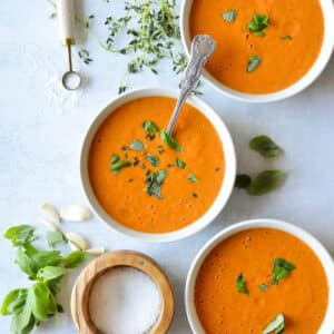 three bowls of cherry tomato soup with basil on top.