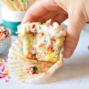 hand holding a gluten free funfetti cupcake with a bite out of it.