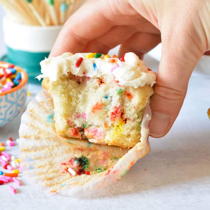 hand holding a gluten free funfetti cupcake with a bite out of it.