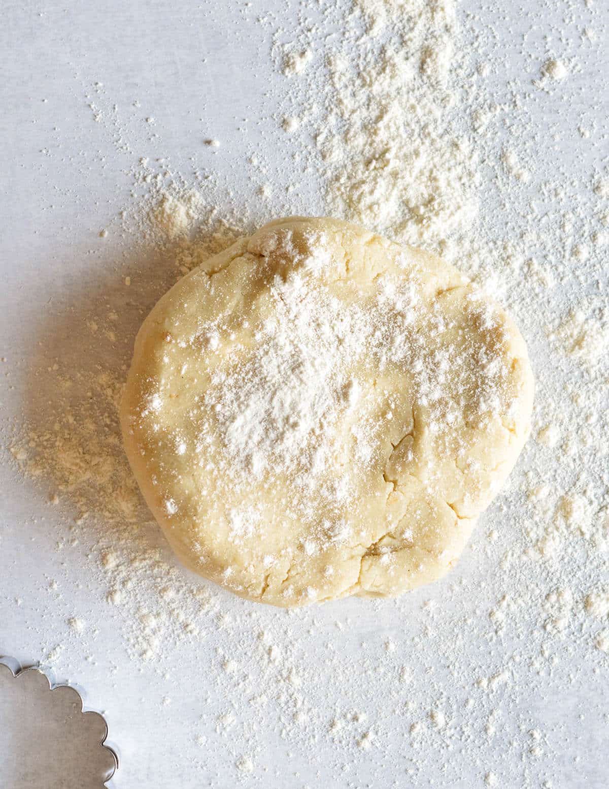 a round disc of gluten-free shortbread dough on a workspace with gluten-free flour