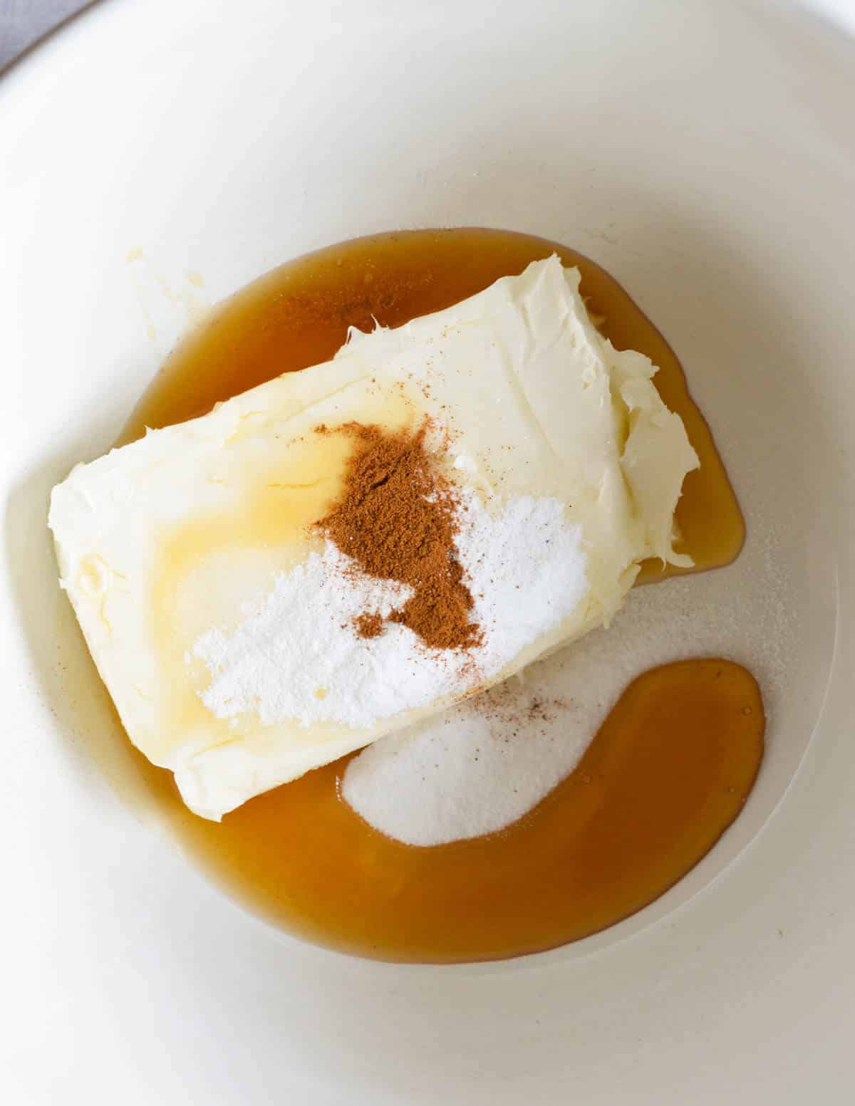 a block of cream cheese, powdered sugar, cinnamon, and honey in a large bowl.