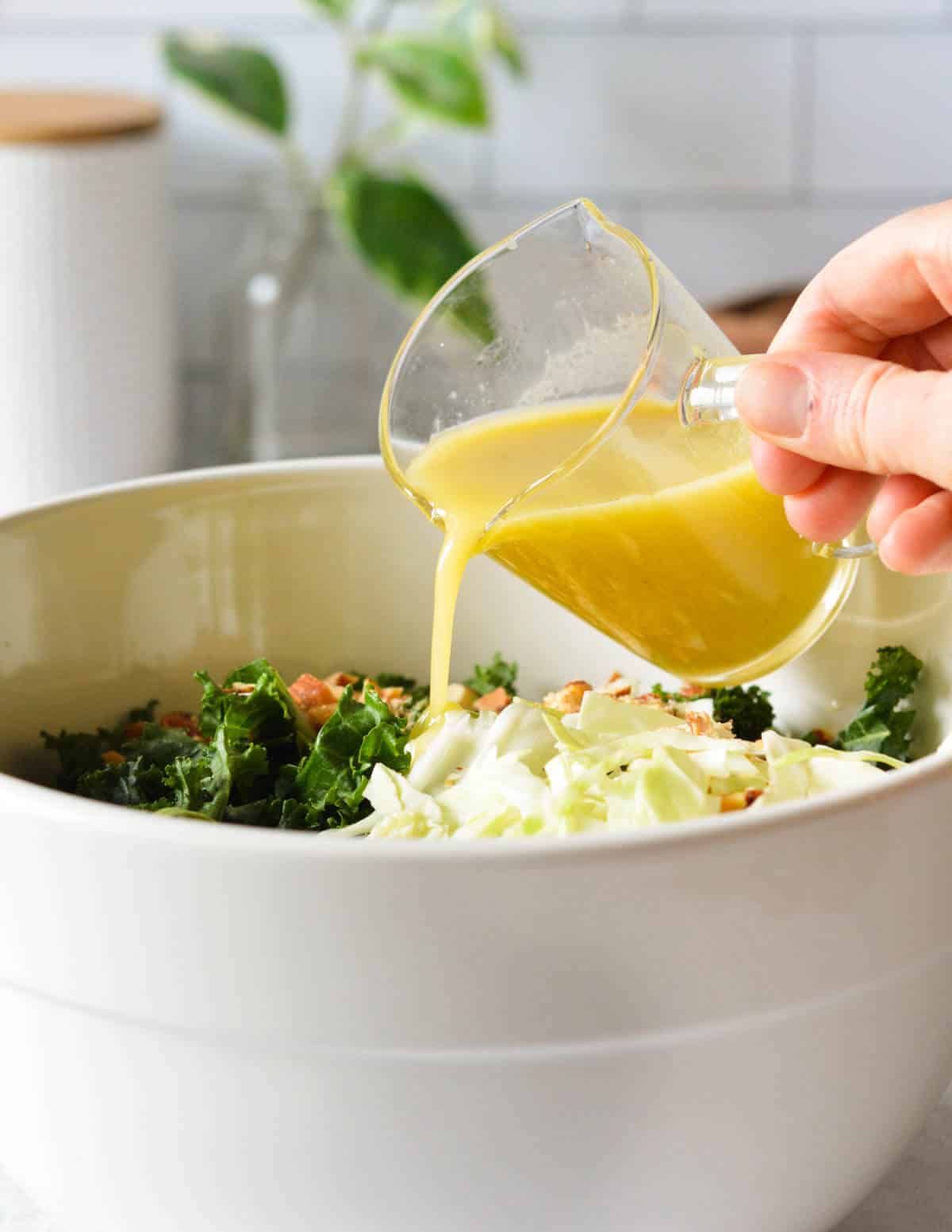 hand pouring an apple dijon vinaigrette onto a kale salad.