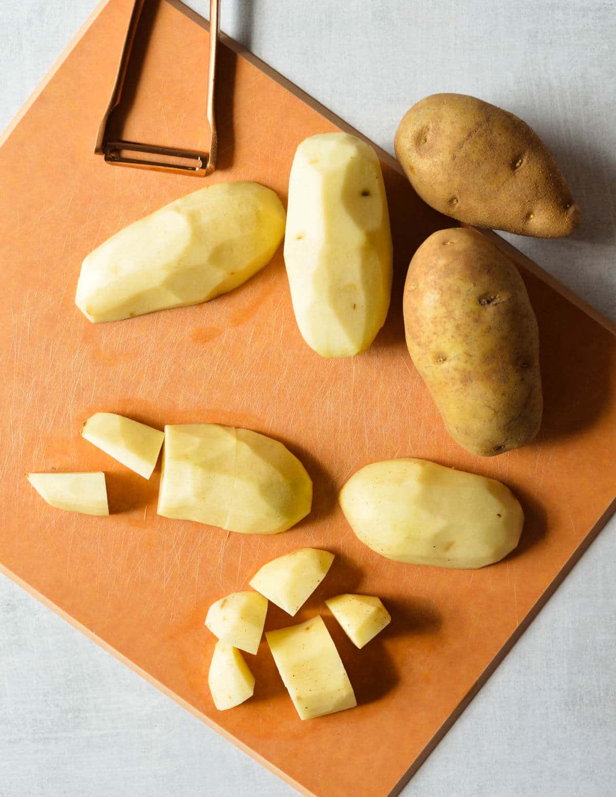 russet potatoes on a cutting board, some cut into chunks.